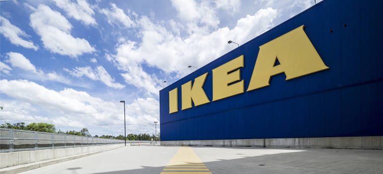 Exterior view of an IKEA store with a large blue wall, yellow logo, and an empty parking lot.