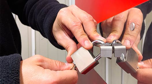 Picture of the hands of a person locking a metal padlock on a door's latch.