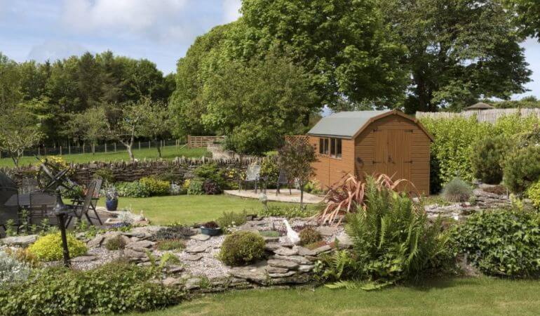 Lush garden with stone paths, a wooden shed, and various plants.