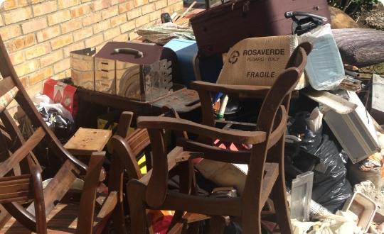 A pile of trash, including wooden chairs and boxes stacked against a brick wall.