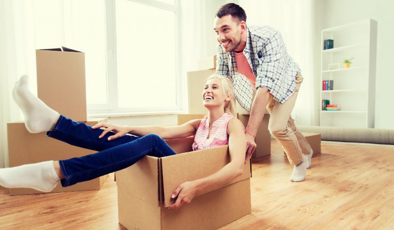 A playful scene with an adult pushing a cardboard moving box with another person sitting inside.